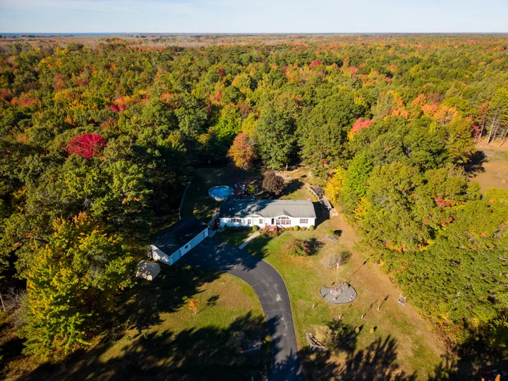 Drone view of the home surrounded by autumn woods